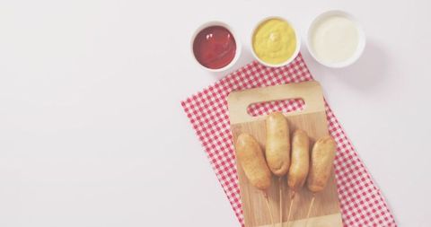 Serving golden corn dogs on wooden board with ketchup, mustard and mayo flatlay