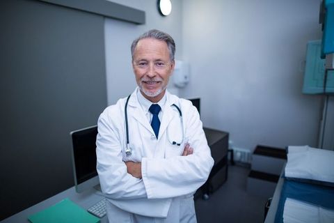 Confident Senior Doctor Crossing Arms in Modern Examination Room