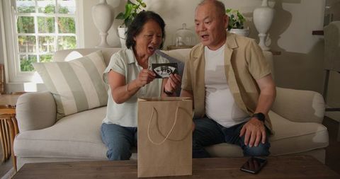Joyful grandparents receiving pregnancy news with gift exchange