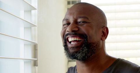 Joyful Man Laughing by Sunlit Window, Modern Home Interior