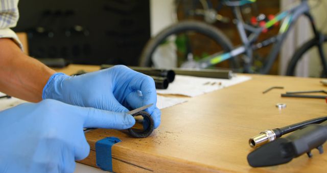 Person wearing gloves working on bicycle part at workshop table filled with tools. Can be used for illustrating concepts like bicycle maintenance, professional repairs, technical expertise, cycle shop operations, and hands-on mechanical work.