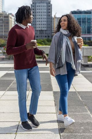 Walking and chatting on urban rooftop plaza holding coffee cups, casual diverse couple