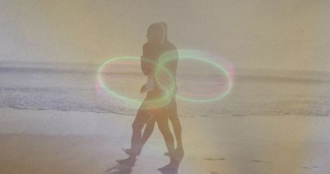 Couple walking on wet sand at sunset with neon light rings silhouetted backlit embrace