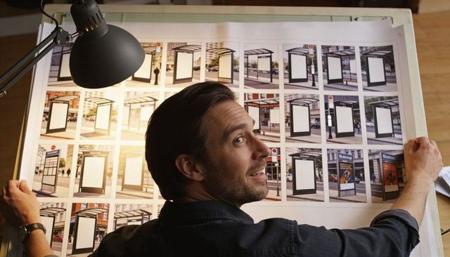 Designer inspecting transit advertising mockup grid on studio drafting table