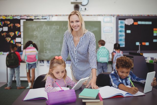 Teacher assisting young students with homework in a classroom full of engaged children. Ideal for educational content, school advertisements, teaching resources, and articles on modern education and classroom environments.