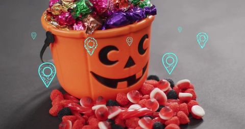 Orange jack-o'-lantern candy bucket overflowing with foil sweets and red gummy treats