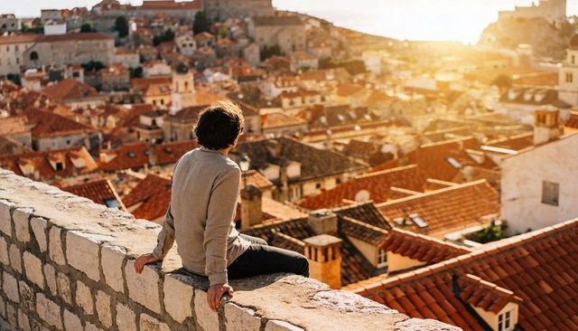 Man sitting on stone wall gazing over terracotta rooftops during golden hour in historic town