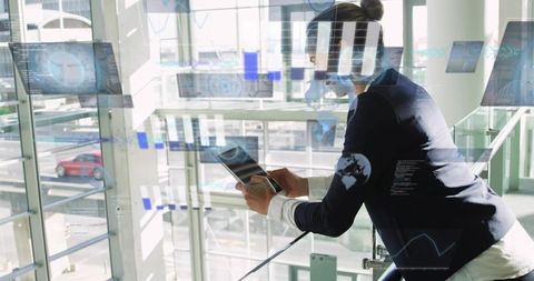 Executive leaning on glass balustrade using tablet with futuristic data hud overlays