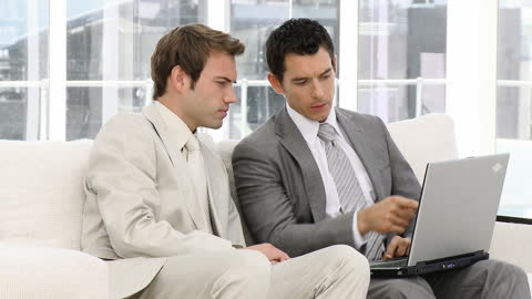Businessmen Collaborating on Laptop in Office Lounge