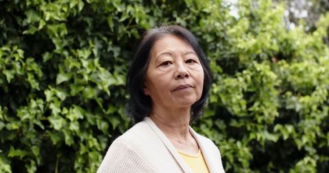 Senior woman relaxing in lush garden wearing cozy sweater