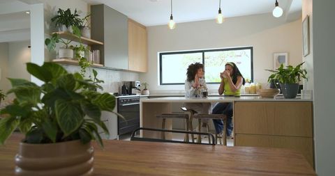 Two diverse women chatting and sipping coffee at modern kitchen island