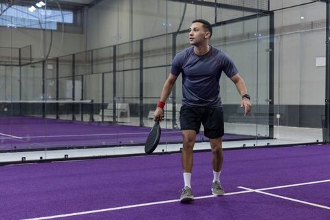 Male athlete playing padel on purple indoor court with glass walls and training focus