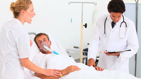 Doctors Monitoring Unconscious Patient in Hospital Bed