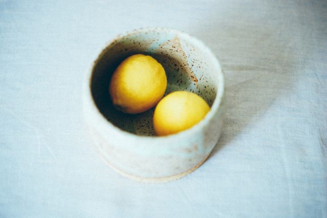 This depicts vibrant yellow lemons inside a rustic ceramic bowl placed on a light linen cloth. Suitable for use in culinary blogs, healthy living websites, natural home decor promotions, and kitchen-related content. Highlights freshness and minimalist lifestyle.