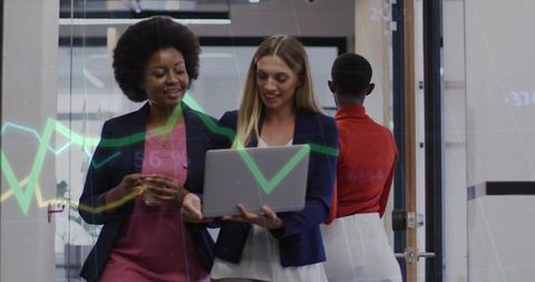 Businesswomen collaborating over laptop with digital analytics overlay in modern office