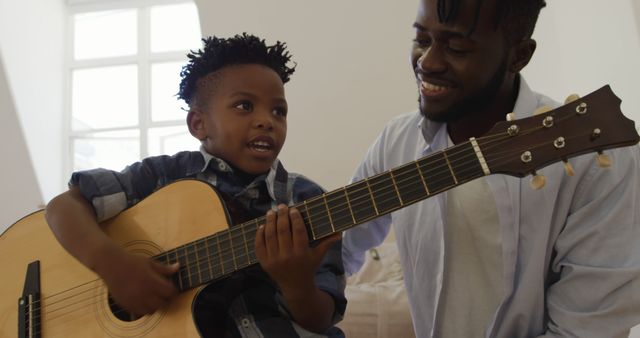 Father and son spending quality time together with a guitar. Ideal for themes like family bonding, music education, and home activities. Perfect for promoting parenting roles, musical instrument learning, and family lifestyle.