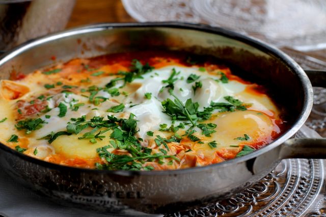 Shakshuka is a delicious, savory dish of poached eggs in a rich tomato sauce, garnished with fresh herbs, served sizzling in a skillet. Great for breakfast, brunch, or dinner. Perfect for food articles, recipe blogs, culinary websites, or menu design.