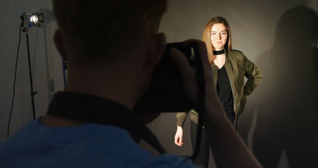 Photographer taking a picture of a young woman who is posing confidently. Suitable for content related to professional photography, modeling careers, fashion shoots, creative industries, portfolio development, and tutorial blogs on how to set up studio lighting.