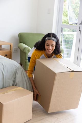 Teenage girl lifting moving box in bright bedroom during home move and unpacking