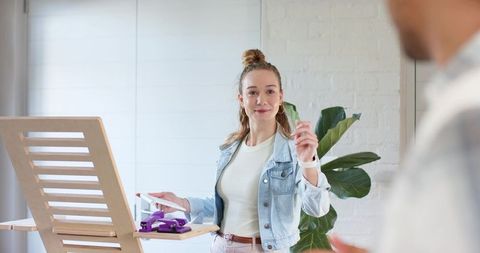 Woman presenting product prototype on easel in home studio for creative collaboration