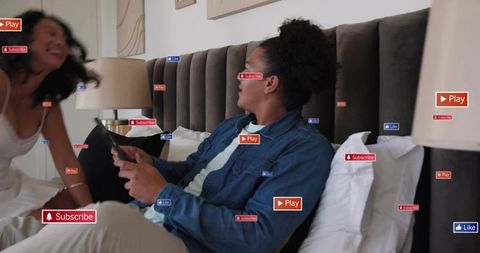 Couple relaxing in bedroom sharing tablet while social media buttons floating around