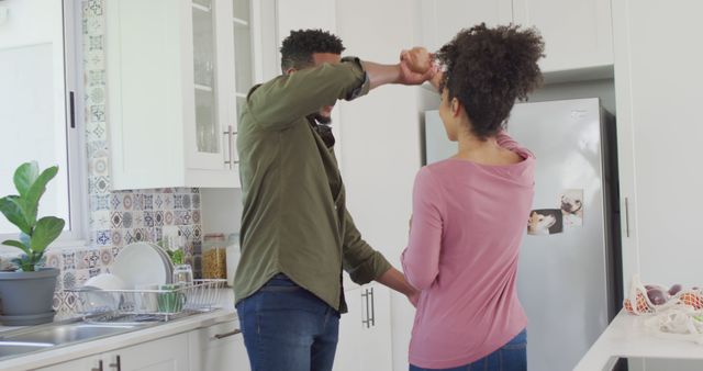 Happy african american couple dancing and holding hands in kitchen. Spending quality time at home together concept.