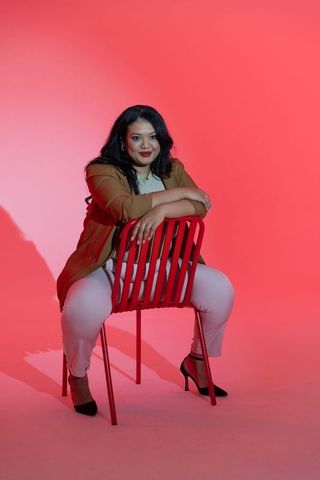 Confident indian businesswoman leaning on red chair, bold studio portrait for branding