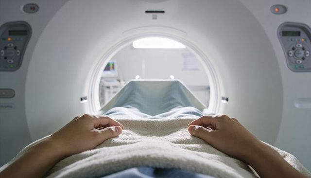 Patient sliding into ct scanner tunnel while lying on table with gown and blanket