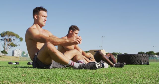 Group of men engaging in an outdoor workout session under sunny conditions. They are performing exercises with weights on a grassy field. The environment is conducive to team fitness activities and depicts a healthy and active lifestyle. Suitable for use in fitness advertisements, outdoor activity promotions, health and wellness content, and team-building exercise features.