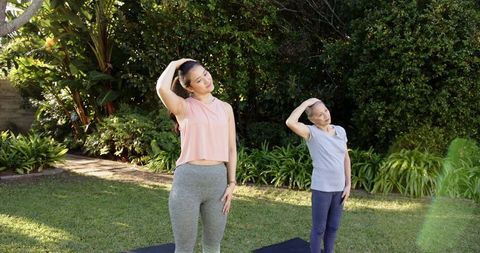 Asian mother and daughter practicing neck stretches in garden