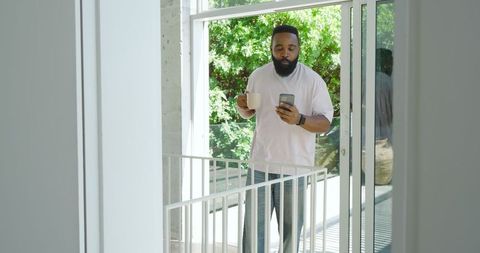 Mid Adult Man Relaxing on Balcony with Coffee and Smartphone