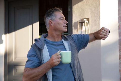 Senior Man Holding Mug on Porch Checking Time