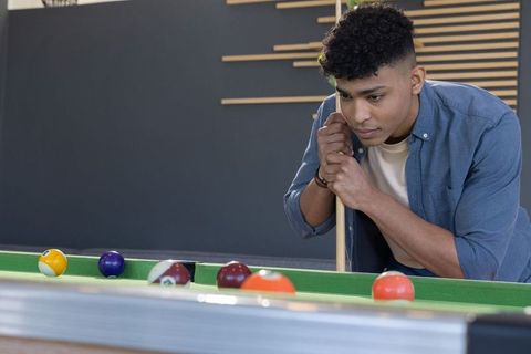 Focusing young man aiming cue on pool table in modern lounge with wood slat accent wall