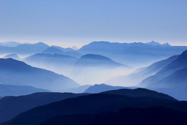 Layers of mountains stretch into the distance, shrouded in mist and bathed in soft blue light at dawn. Ideal for use in nature-themed publications, travel advertisements, or as a calming wall art piece.