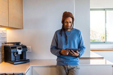 African american man leaning on modern kitchen counter using tablet by espresso machine