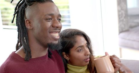 African American Man and Indian Woman Relaxing on Sofa, Sharing Morning Coffee and Smile