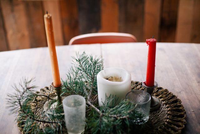 Rustic holiday decoration on a wooden table features candles surrounded by a wreath of pine branches, creating a cozy farmhouse ambiance. This setup is ideal for holiday-themed websites, seasonal decorations advertisements, and home decor promotions.