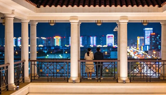 Couple gazing over city nightscape from columned terrace balcony with decorative railings