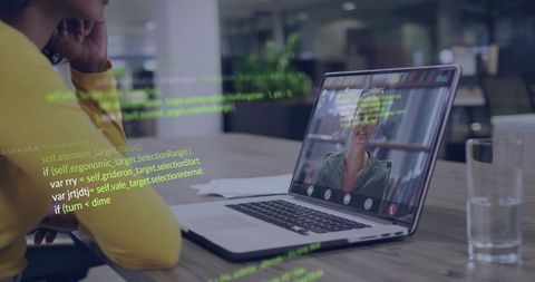 Woman wearing yellow sweater watching laptop during video call with software code overlay
