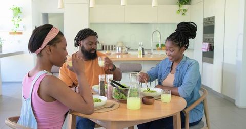 African family sharing healthy salad lunch and fresh juice around wooden kitchen table