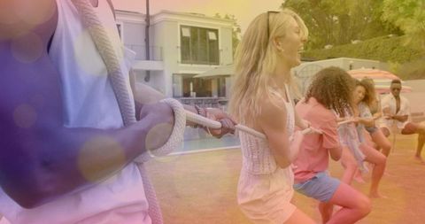Playing tug-of-war beside pool during summer backyard party with diverse friends