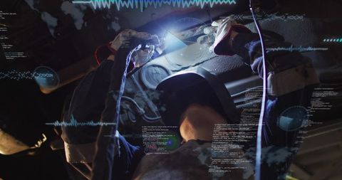 Female welder welding under vehicle in garage with digital code overlay suggesting automotive tech
