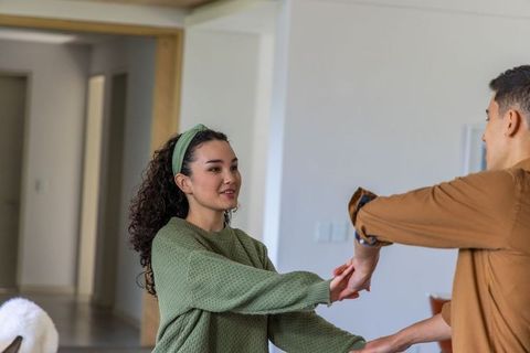 Couple holding hands and dancing in cozy home, woman in green sweater smiling