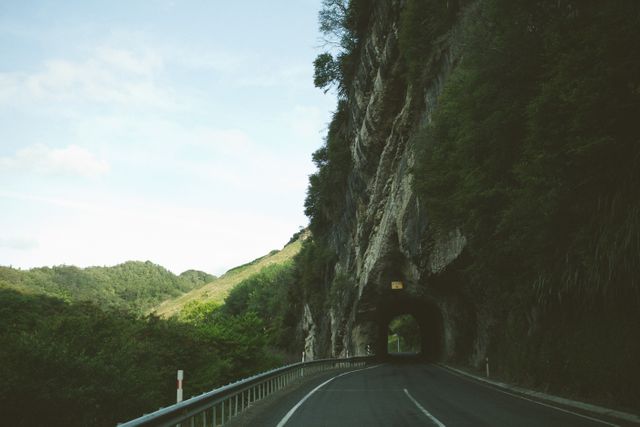Depicts a scenic road passing through a tunnel carved in a rocky mountain. Ideal for use in travel blogs, road trip promotions, and adventure travel advertisements. Highlights the natural beauty and unique travel experience.