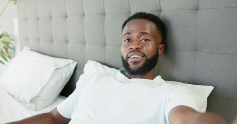 Afroamerican Man Relaxing in Modern Bedroom with Smartphone