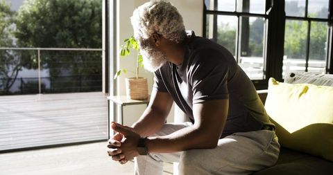 Senior man reflecting by sunlit patio windows