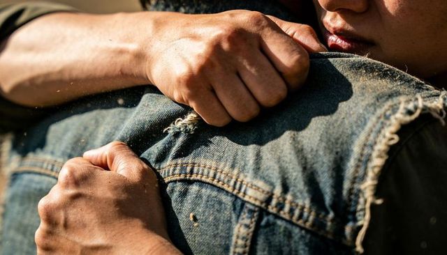 Closeup hands embracing frayed denim jacket, sunlit dust particles, intimate connection
