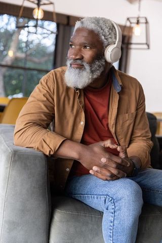 Senior african american man listening with headphones on sofa in cozy modern lounge