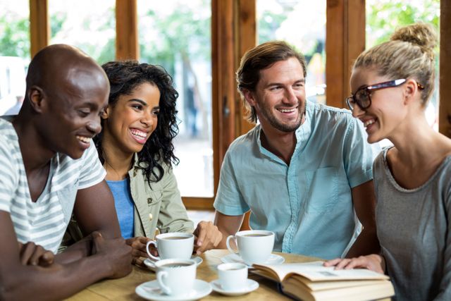 Group of friends sitting at a table in a cozy cafe, enjoying coffee and engaging in lively conversation. Ideal for use in advertisements, social media posts, and articles about friendship, social gatherings, and multicultural interactions.