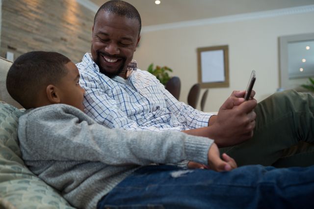Father and son using mobile phone on sofa in living room at home